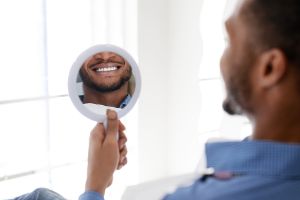 Man holding up a mirror, looking at his teeth in the dentist's office.