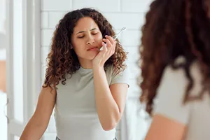 Person holding hand to mouth in discomfort from tooth sensitivity.